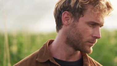 A close-up view of a handsome farmer is posing to the camera walking at the greenhouse