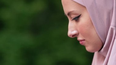 Pembe başörtüsü takan Arap bir kadının yakın plan görüntüsü şehir parkında otururken dizüstü bilgisayarını kullanıyor.