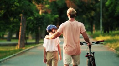 Küçük oğluyla birlikte bir babanın arka görüntüsü yazın parkta bisiklete binecek.