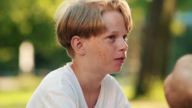 Küçük bir çocuğun yakın çekim görüntüsü yazın parkta çimlerin üzerinde piknik yaparken konuşuyor.