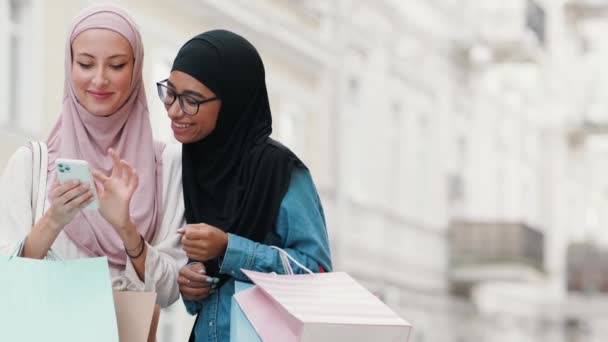 ヒジャーブを着た明るいアラビア人女性が買い物の後に外を歩いている間に携帯電話を使用しています — ストック動画