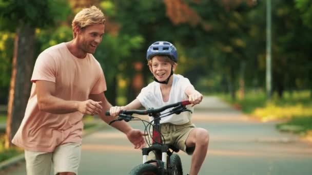 Счастливый Отец Учит Своего Маленького Сына Кататься Велосипеде Помогая Ему — стоковое видео