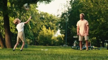 Mutlu bir baba ve oğlu yazın parkta badminton oynuyorlar.