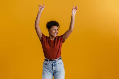 Happy casually dressed young african woman standing over yellow wall background, dancing