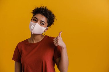 Young black woman in face looking at camera and showing thumb up isolated over yellow background