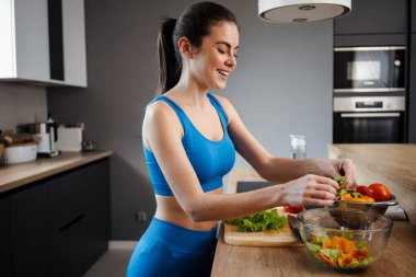 Beyaz esmer kadın evde salata yaparken gülümsüyor.