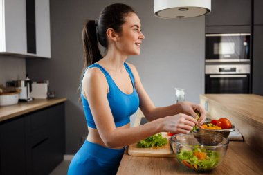 Beyaz esmer kadın evde salata yaparken gülümsüyor.