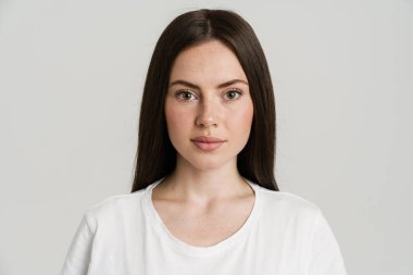 Genç esmer kadın poz veriyor ve beyaz arka planda izole edilmiş kameraya bakıyor.