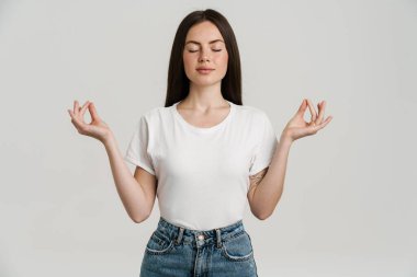 Genç esmer kadın, meditasyon yaparken gözleri kapalı, beyaz arka planda izole bir şekilde el kol hareketi yapıyor.