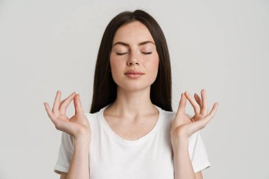 Genç esmer kadın, meditasyon yaparken gözleri kapalı, beyaz arka planda izole bir şekilde el kol hareketi yapıyor.