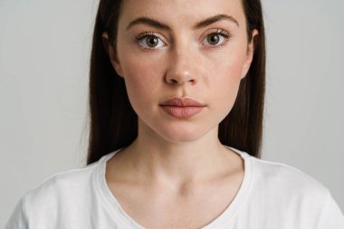 Genç esmer kadın poz veriyor ve beyaz arka planda izole edilmiş kameraya bakıyor.