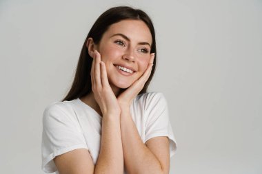 Tişörtlü genç esmer kadın gülümsüyor ve beyaz arka planda soyutlanmış bir şekilde yan tarafa bakıyor.