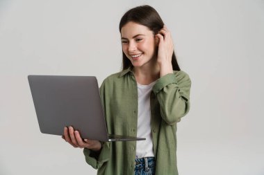 Genç esmer kadın gülümserken beyaz arka planda dizüstü bilgisayarla poz veriyor.