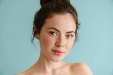 Yarı çıplak esmer kadın. Mavi arka planda yalnız poz verip kameraya bakıyor.