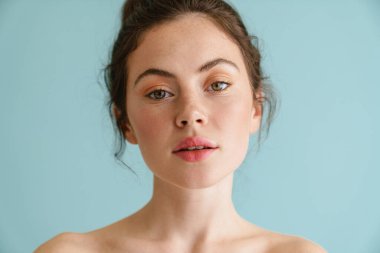 Yarı çıplak esmer kadın. Mavi arka planda yalnız poz verip kameraya bakıyor.