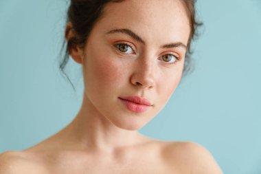 Yarı çıplak esmer kadın. Mavi arka planda yalnız poz verip kameraya bakıyor.