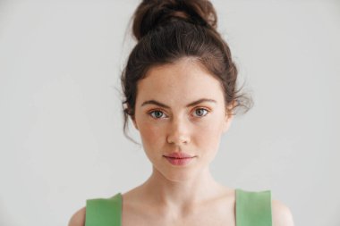 Oldukça ciddi esmer bir kadın poz veriyor ve beyaz arka planda izole edilmiş kameraya bakıyor.