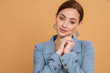 Ceketli genç kızıl kadın gülümsüyor ve sarı arka planda izole edilmiş kameraya bakıyor.