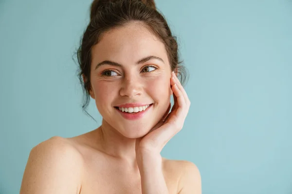 Half-naked brunette woman smiling and looking aside isolated over blue background