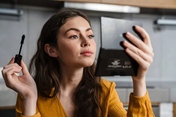 Sonriente Joven Morena Haciendo Maquillaje Mientras Está Sentada Cocina Casa —  Fotos de Stock