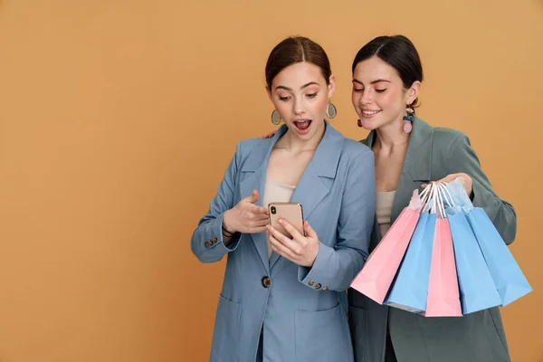 Jovens Duas Mulheres Segurando Sacos Compras Usando Celular Isolado Sobre — Fotografia de Stock