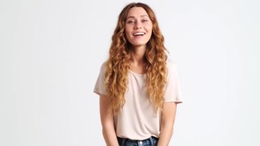 Mutlu bir kadın kameraya bakıyor. Stüdyodaki beyaz duvarın üzerinde tek başına duruyor.