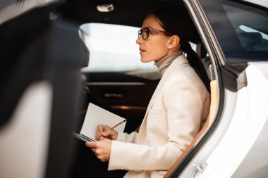 Güzel odaklı iş kadını arabada otururken notlar yazıyor.