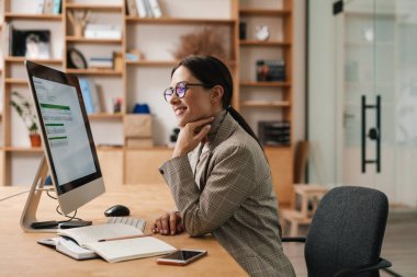 Ofiste bilgisayar ve takvimle çalışan, gözlüklü, gülümseyen çekici kadın.