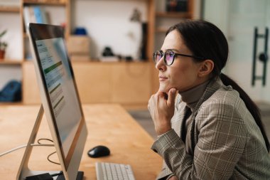Ofiste otururken bilgisayarla çalışan gözlüklü çekici bir kadın.