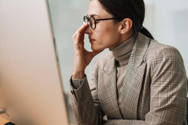 Ofiste bilgisayarla çalışan baş ağrısı olan yorgun ve çekici bir kadın.