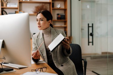 Ofiste bilgisayarla konferans görüşmesi yaparken planlayıcısını gösteren odaklanmış bir kadın.