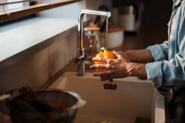 Beyaz kadın ev mutfağında sebze yıkıyor.