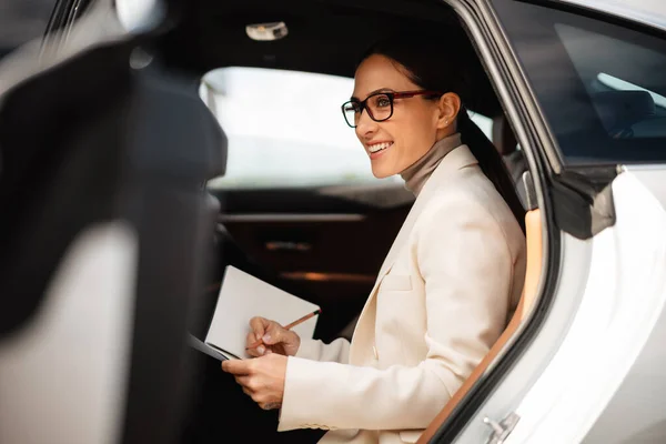 Mulher Negócios Feliz Bonita Sorrindo Escrevendo Notas Enquanto Sentado Carro — Fotografia de Stock