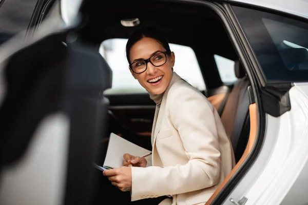 Mulher Negócios Feliz Bonita Sorrindo Escrevendo Notas Enquanto Sentado Carro — Fotografia de Stock