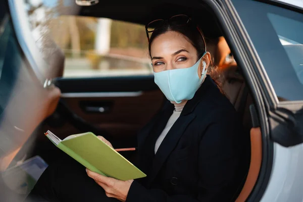 Foto Koncentrerad Affärskvinna Sitter Bil Ansiktsmask Medan Håller Anteckningsbok — Stockfoto