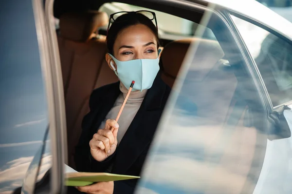 Foto Koncentrerad Affärskvinna Sitter Bil Ansiktsmask Medan Håller Anteckningsbok — Stockfoto