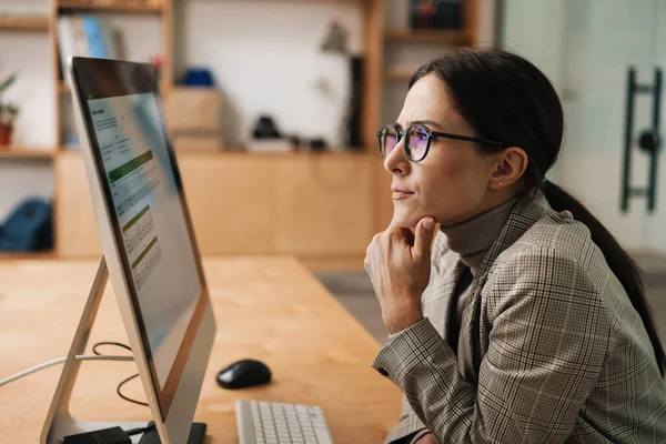 Ofiste otururken bilgisayarla çalışan gözlüklü çekici bir kadın.