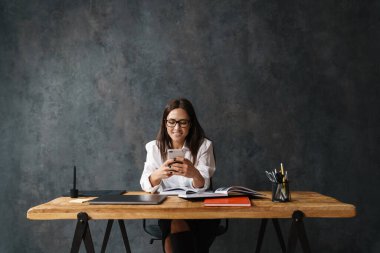 Gülümseyen yaşlı iş kadını. Masanın arkasında otururken cep telefonu kullanıyor.