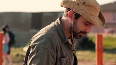 Çiftçinin yakın plan görüntüsü bir keçiyi okşarken keçi çiftliğinin önünde dikiliyor.