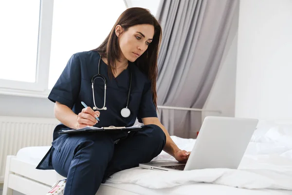 Doctora Enfocada Con Escritura Estetoscopio Mientras Trabaja Con Computadora Portátil — Foto de Stock