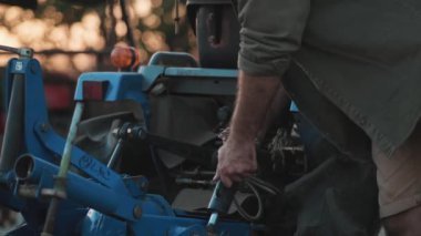Şapkalı bir çiftçinin yakın planda çekilmiş görüntüsü traktörünü bir köyde işe hazırlıyor.