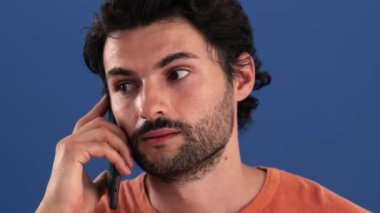 Mobil telefonuyla konuşan mutlu esmer bir adamın yakın çekim görüntüsü stüdyonun mavi arka planında izole bir şekilde duruyor.