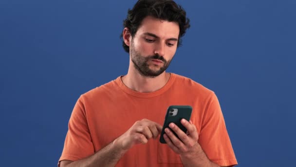 Yakışıklı Bir Esmer Adam Cep Telefonunu Kullanarak Stüdyonun Mavi Arka — Stok video
