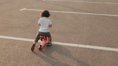 Küçük bir çocuk park yerinde üç tekerlekli bisikletine biniyor.