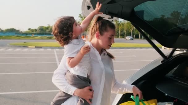 車のトランクから物事を取りながら 母親は彼女の手に彼女の赤ちゃんの男の子を保持している — ストック動画