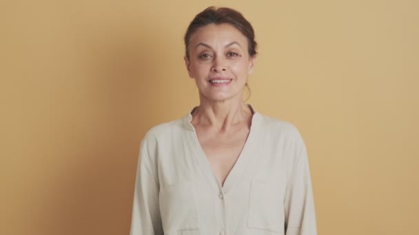 Medelålders Brunett Kvinna Ler Mot Kameran Stående Isolerad Över Beige — Stockvideo