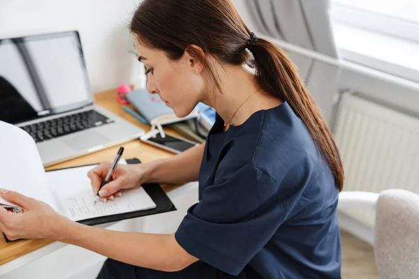 Zaostřená Žena Lékař Pracuje Notebookem Papíry Zatímco Sedí Stolu Doma — Stock fotografie