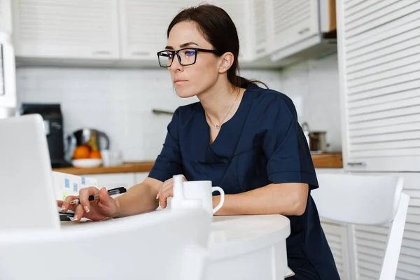 Žena Modrém Lékařském Obleku Brýlích Sedící Stolu Před Laptopem Dívající — Stock fotografie