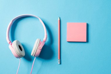 Mavi bir stüdyoda duran bir kulaklık, bir kağıt ve bir kalem.