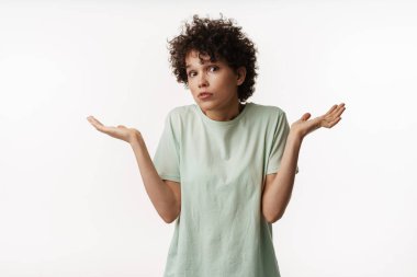 Şaşırmış kıvırcık esmer kadın somurtuyor ve telif alanını beyaz arka planda yalnız tutuyor.